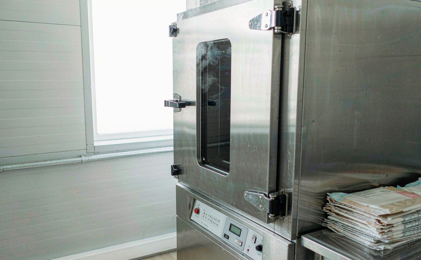 A stainless steel benchtop autoclave with its door ajar and sealed sterilization pouches stacked beside it