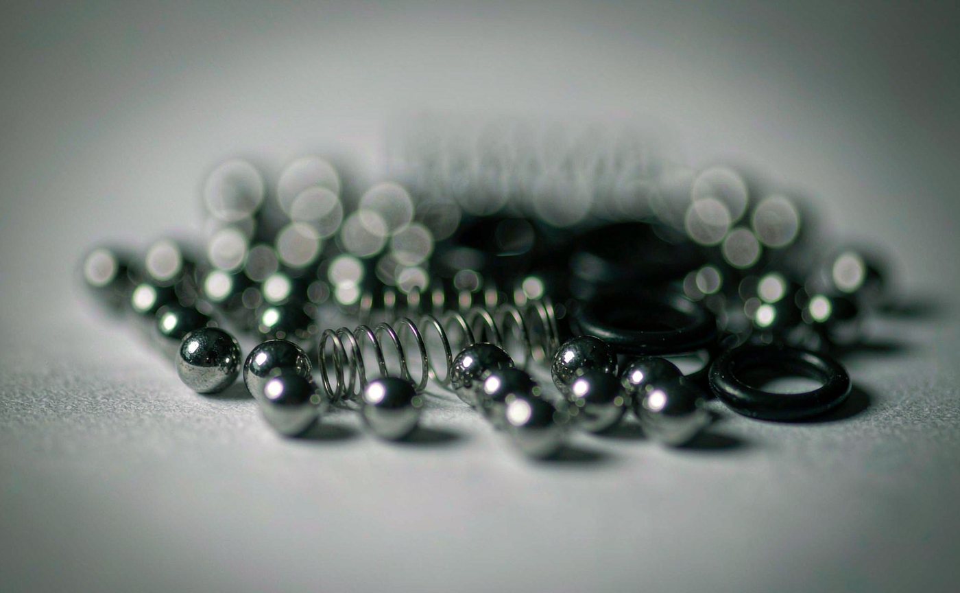 Extreme close-up of miniature steel ball bearings, coil springs and rubber O-rings on a grey surface